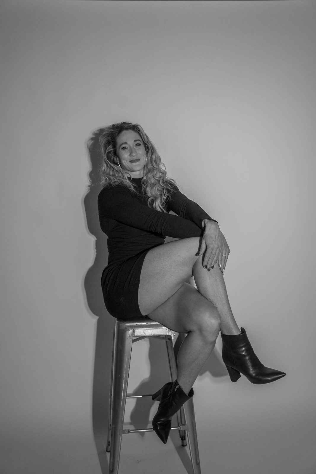 Perched on a stool with legs crossed, high-key black and white