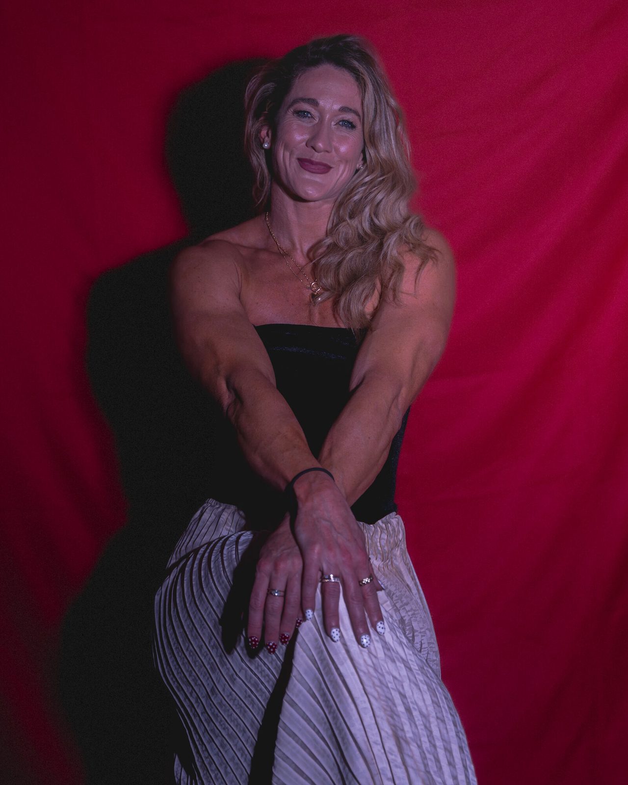 Seated against a deep-red backdrop in a strapless top and pleated skirt
